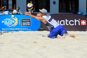 Beach volley -pelaaja polvillaan hiekassa lyömässä palloa