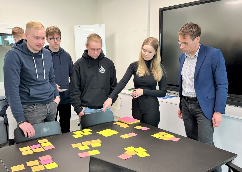 Viisi henkilöä katsoo pöydän ympärillä pöydälle levitettyjä post-it-lappuja