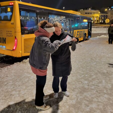 Minttu Tuominen ja Anna Kilponen katsovat karttaa keltaisen bussin edessä talvivaatteet päällä. Bussissa on islanninkielistä tekstiä.