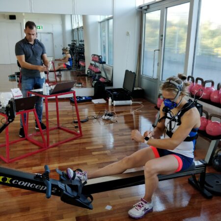 Tuuli Petäjä-Sirén sitting on a rowing ergometer with oxygen mask on, tester is next to her having two computers in front of him.