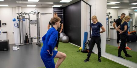 Urheilija tekee askelkyykkyä fysioterapeutin katsellessa vierestä