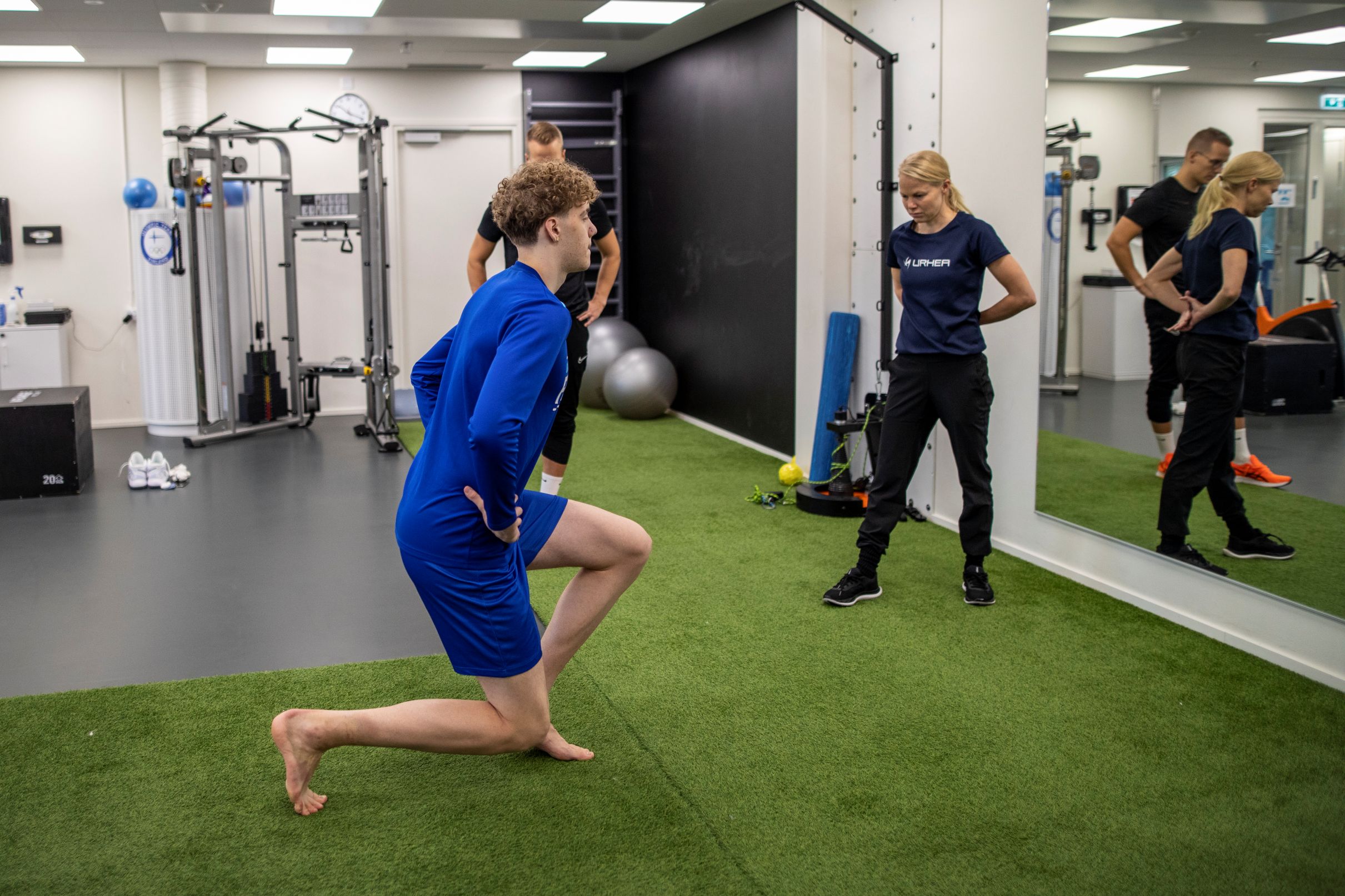 Urheilija tekee askelkyykkyä fysioterapeutin katsellessa vierestä