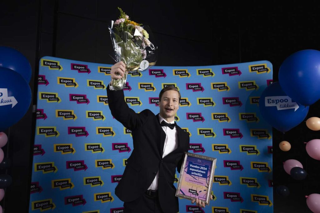 Justus Kainulainen pitää kädessään kunniakirjaa ja toisessa kädessään kukkakimppua